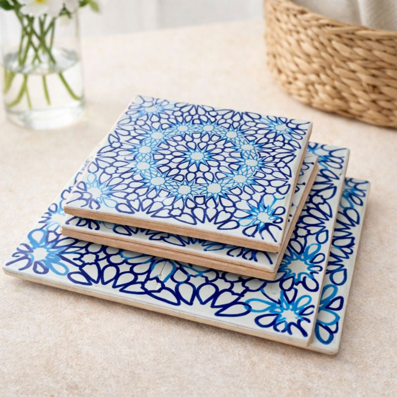 Set of three ceramic coasters with blue floral patterns on a beige surface.